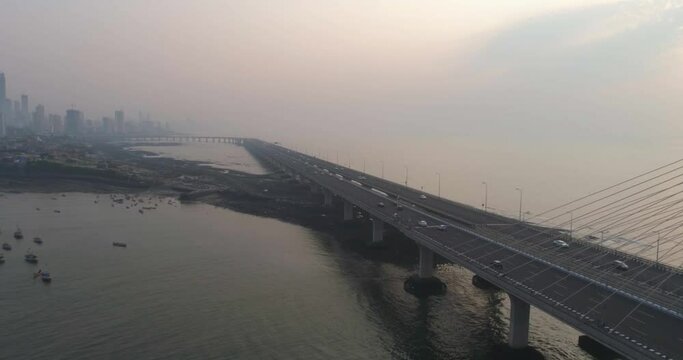 A drone shot at Bandra Worli Sea Link seen from an aerial view in slow motion. Cinematic drone movement with the iconic Mumbai Sea Link at the forefront and the city view in the background.