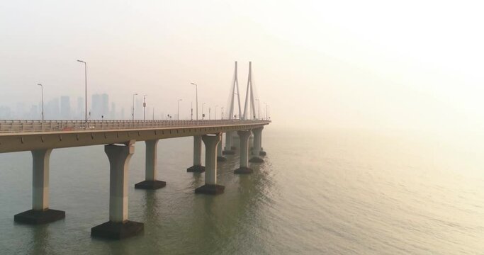 A drone shot at Bandra Worli Sea Link seen from an aerial view in slow motion. Cinematic drone movement with the iconic Mumbai Sea Link at the forefront and the city view in the background.