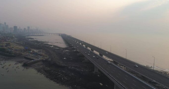 A drone shot at Bandra Worli Sea Link seen from an aerial view in slow motion. Cinematic drone movement with the iconic Mumbai Sea Link at the forefront and the city view in the background.
