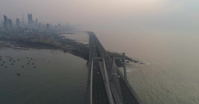 A drone shot at Bandra Worli Sea Link seen from an aerial view in slow motion. Cinematic drone movement with the iconic Mumbai Sea Link at the forefront and the city view in the background.