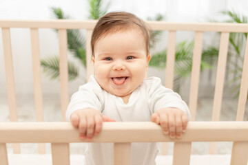 happy baby shows tongue while standing in the crib