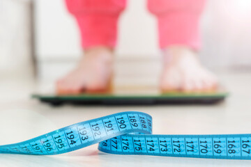 a woman standing on a floor scale in the room. Overweight problem, body measurement tape before weights