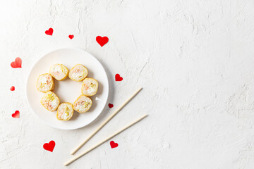 Sushi for Valentine's Day with red hearts and chopsticks on a white plate. Horizontal orientation, copy space, top view.