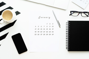 Calendar of February on white desktop flat lay with a cup of coffee and a notebook, work space