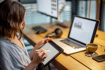 Young woman dressed casually having some creative work, drawing on a digital tablet, sitting at the...