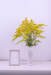 bouquet of yellow flowers in a white vase and photo frame