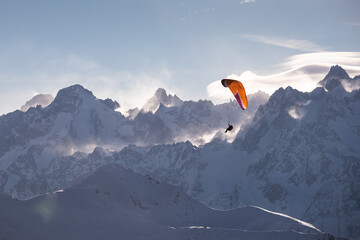 Parasailor glides over snowcapped mountains and lofty clouds