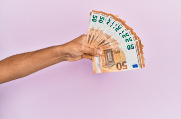 Hispanic hand holding 50 euro banknotes over isolated pink background.