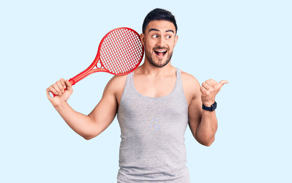 Young handsome man holding tennis racket pointing thumb up to the side smiling happy with open mouth