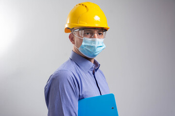 Fototapeta na wymiar Portrait of an handsome engineer with face mask and blue clipboard isolated on grey