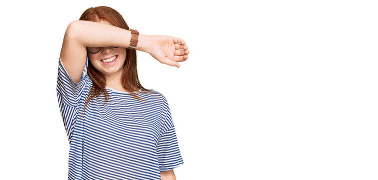 Young read head woman wearing casual clothes and glasses covering eyes with arm smiling cheerful and funny. blind concept.