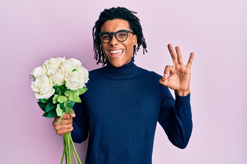 Young african american man holding bouquet of white flowers doing ok sign with fingers, smiling friendly gesturing excellent symbol