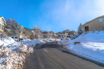 Road along homes with snowy yards against blue sky on a scenic winter landscape