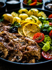Fototapeta na wymiar Fried pork steaks with lemon, boiled potatoes and vegetable salad served on wooden table 