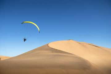 Fototapeta na wymiar Parasailor lands on giant sand dunes