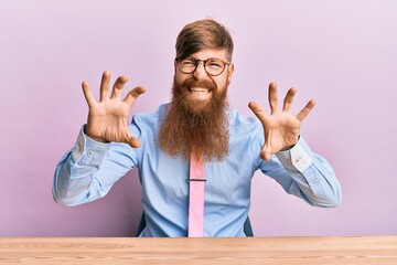 Young irish redhead man wearing business shirt and tie sitting on the table smiling funny doing...