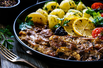 Fried pork steaks with lemon, boiled potatoes and vegetable salad served on wooden table
