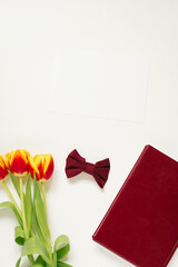 Background to Valentine's Day. Mother's Day or Spring. Burgundy notebook, bow, flowers on a white background, top view. Free space for the text field, top view. Free space for text