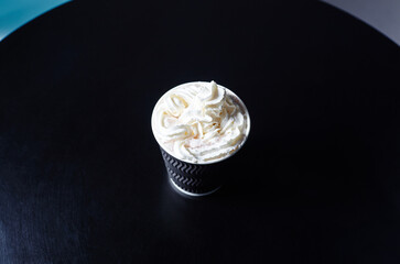 Disposable paper cup with tasty coffee drink with milk and whipped cream on wooden table in cafe