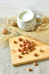 Hazelnuts on a cutting board and cup of milk, wooden background with burlap and a linen napkin.