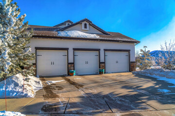 Home with three white hinged garage doors and snowy roof and yard at the facade