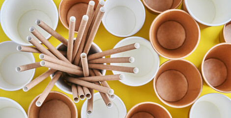 Drinking tubes made of paper and cornstarch, biodegradable material and eco paper glasses with green sprout leaves on yellow trend color 2021 background. Zero waste and plastic free concept. Top view.