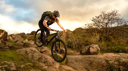 Naklejka premium Professional Cyclist Riding Bike on the Autumn Rocky Trail at Sunset. Extreme Sport and Enduro Biking Concept.