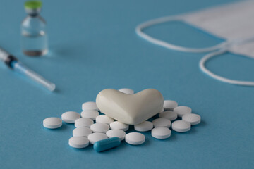 The white heart on pills with masks and syringes on a blue background. 