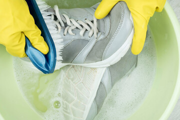 hands in rubber gloves clean sneakers with a brush. Brush and solution of water and detergent. Keep...