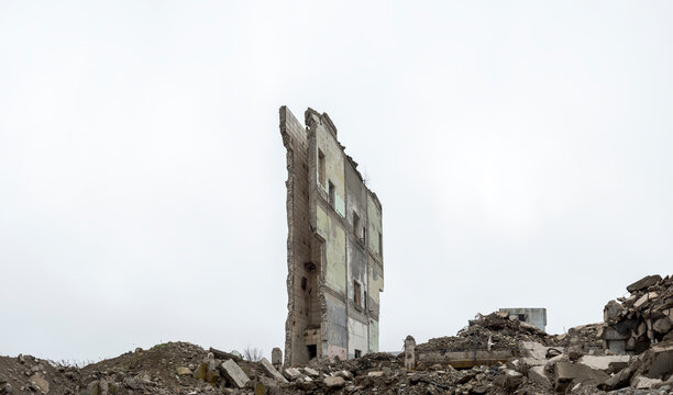 Panorama. Piles of gray concrete rubble and the remains of a collapsed wall against a hazy sky.