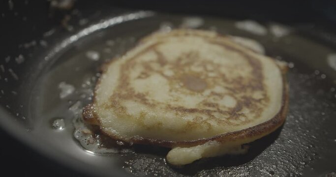 Camera panning over golden pancake baking in a black pan with sizzling oil and silver spatula aside