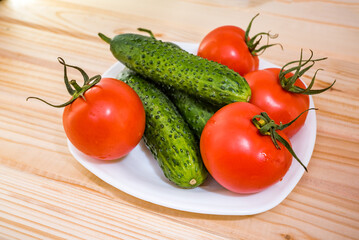 white plate with fresh vegetables from the vegetable garden such as tomatoes and cucumbers on a wooden table.