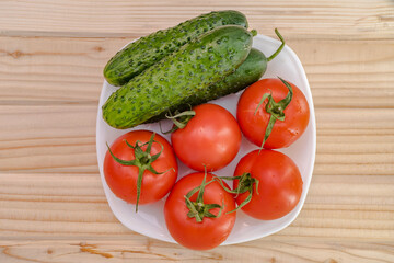 white plate top view of fresh vegetables from the garden such as tomatoes and cucumbers on a wooden table.