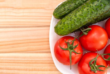 white plate top view on fresh vegetables from vegetable garden such as tomato and cucumber on wooden table close-up.