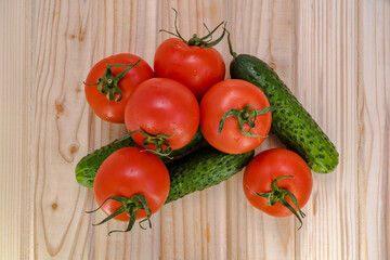 red tomatoes and green cucumbers on a wooden table top view.
