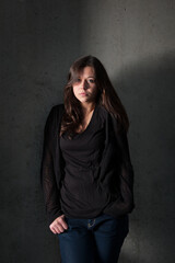 Outdoor portrait of a sad teenage girl wearing blue jeans and black top in front of a gray wall