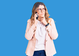 Young caucasian woman having conversation talking on the smartphone serious face thinking about question with hand on chin, thoughtful about confusing idea