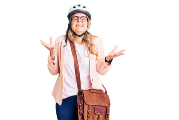 Young caucasian woman wearing bike helmet and leather bag celebrating mad and crazy for success with arms raised and closed eyes screaming excited. winner concept