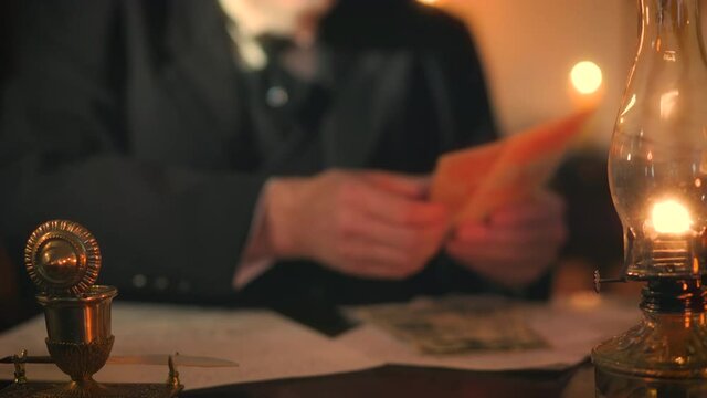 Candlelight and light from oil lamps illuminate the scene of this Victorian era businessman who counts several paper bills and using a dip pen makes notations on a document.