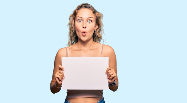 Beautiful caucasian woman holding blank empty banner scared and amazed with open mouth for surprise, disbelief face