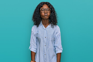 Beautiful african young woman wearing casual clothes and glasses puffing cheeks with funny face....
