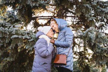 Motherhood. Theme importance visiting and spending time with old single parents during holidays. Senior mom and mature daughter happy family hug and laugh in park background Christmas tree in winter