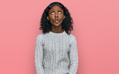 Beautiful african young woman wearing casual winter sweater making fish face with lips, crazy and comical gesture. funny expression.