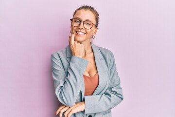 Beautiful caucasian woman wearing business jacket and glasses looking confident at the camera with smile with crossed arms and hand raised on chin. thinking positive.