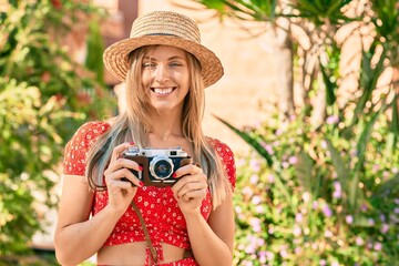Young blonde tourist woman wearing summer style using vintage camera at the park