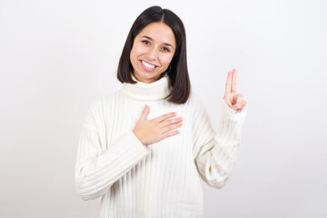 Young brunette woman wearing white knitted sweater against white background smiling swearing with...