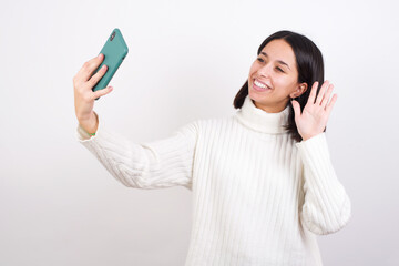 Young brunette woman wearing white knitted sweater against white background smiling and taking a...