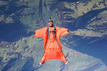Wingsuit flier glides on his back over snowcapped mountains