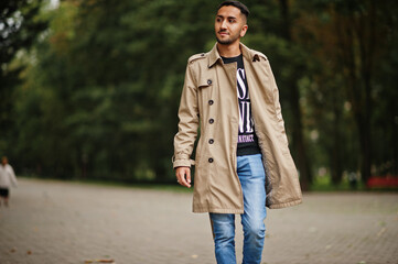 Stylish kuwaiti man at trench coat walking at park.