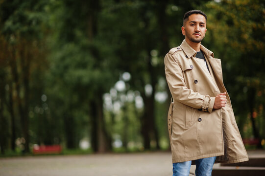 Stylish kuwaiti man at trench coat walking at park.